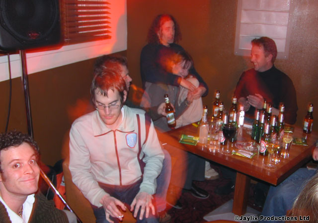 People sit around a table of bottles, one man in a white jacket holding a bottle in the foreground