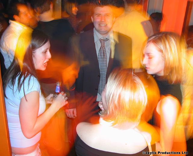 A crowd dances in blurred motion, with a man in a suit and tie in the centre