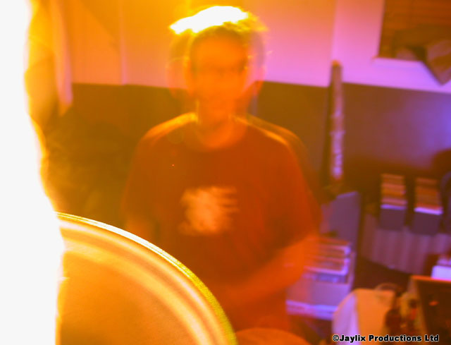 Matt in a dragondrop T shirt behind an out of focus foreground, in orange and purple light