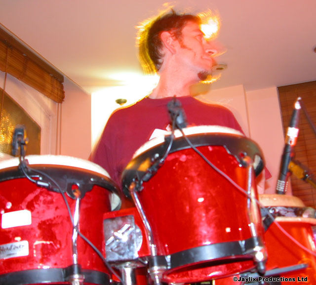 A person with spiky hair plays red bongo drums with microphones in front