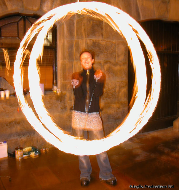 A person stands inside a glowing circle of fire from spinning poi in front of a stone wall