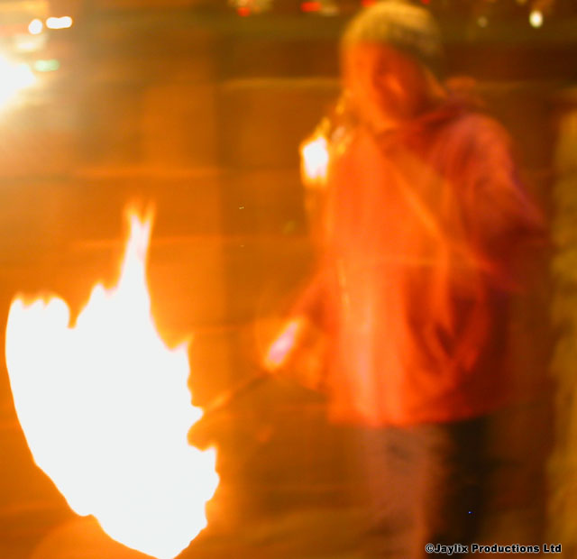 A blurred person stands between two bright flames in orange light