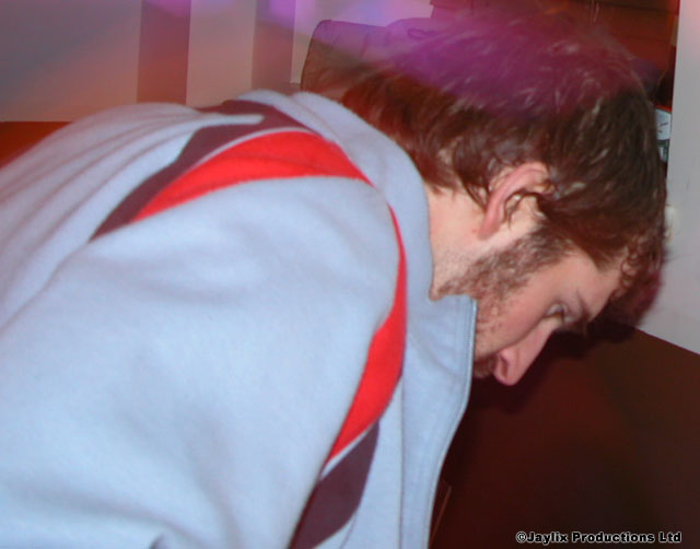 A man with a beard leans forward, head down, in a light blue top with a red stripe