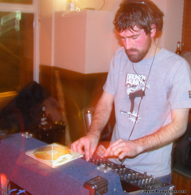 A bearded man wearing headphones mixes records at a DJ desk