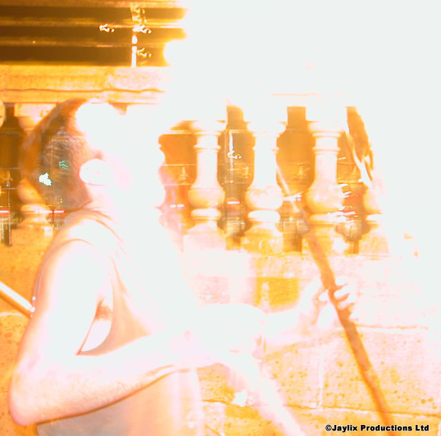 An overexposed, washed out image of a person by a stone balustrade, with a staff, firebreathing