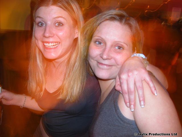 Two women pose close together and smile, in orange light with blur behind