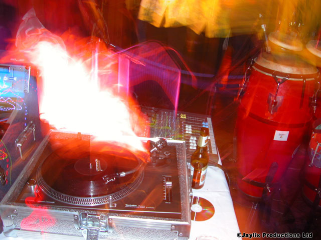 A record deck with a large flame behind it and a red conga drum on the right