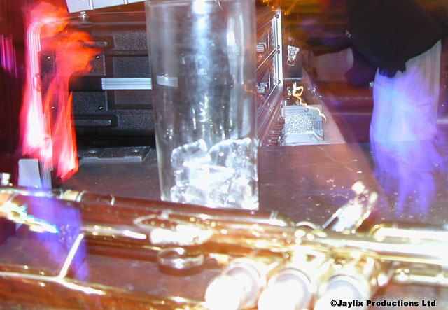A trumpet on a bar beside a tall glass of ice, with blurred equipment behind