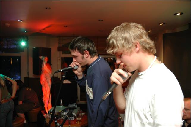 Two beatboxers, one with short dark hair and one with blond hair, hold microphones to their mouths