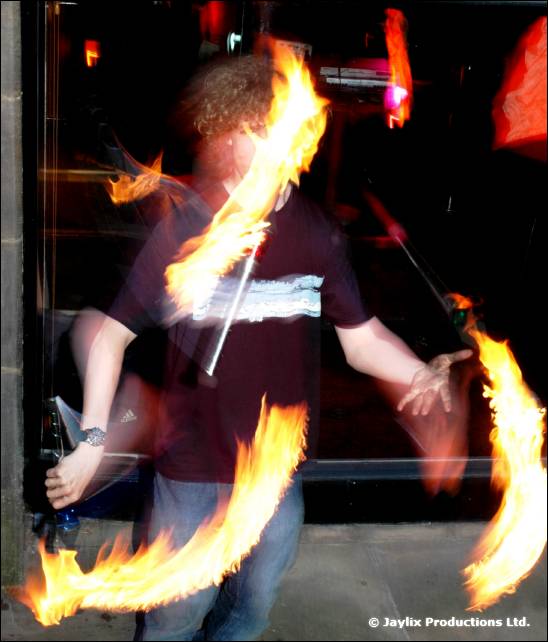 Person in a dark T-shirt spins flaming staffs outdoors at night
