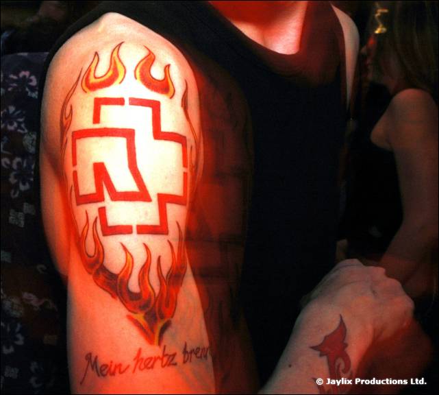 Close view of an upper arm with a red flame and logo tattoo, reading Mein herz brennt
