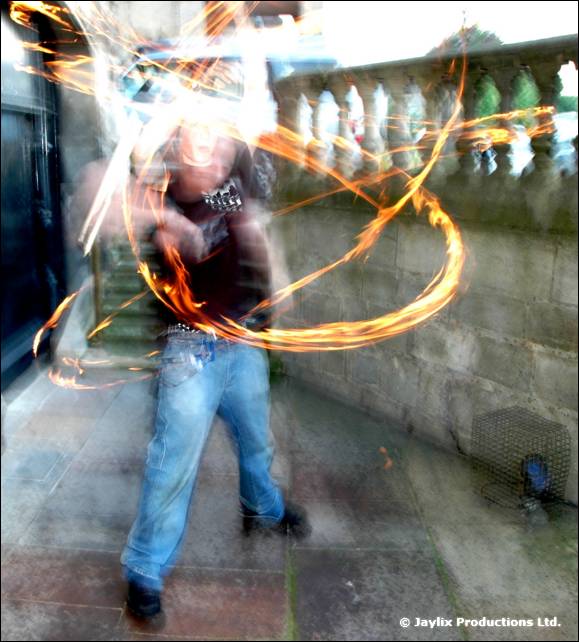 Person in jeans spins fire staffs on a stone terrace with a balustrade behind