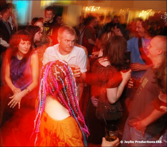 Crowd dancing in a busy bar, with a person with pink and blue dreadlocks in the foreground