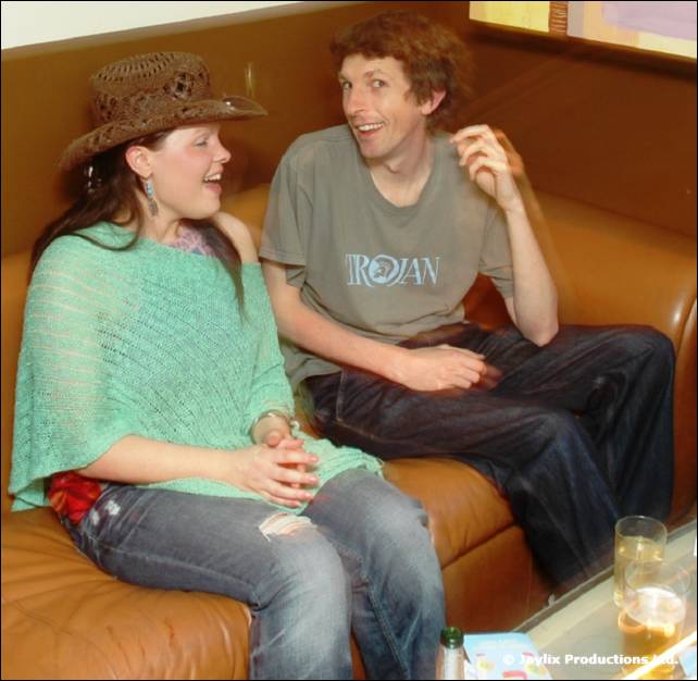 Woman in a straw hat and green top and a man in a grey T-shirt sit on a brown leather sofa