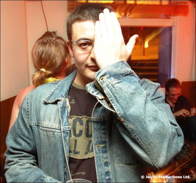 A person in glasses and a denim jacket covers one eye with a hand