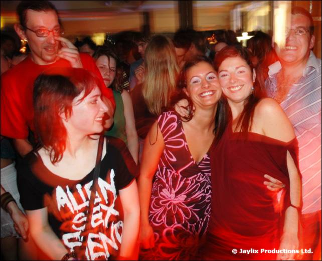 A smiling group of people crowd together in a bar, one wearing a black top printed with white lettering