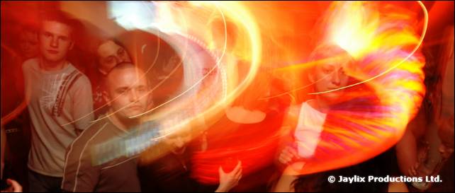 Several blurred people stand in a red-lit crowd with swirling light trails