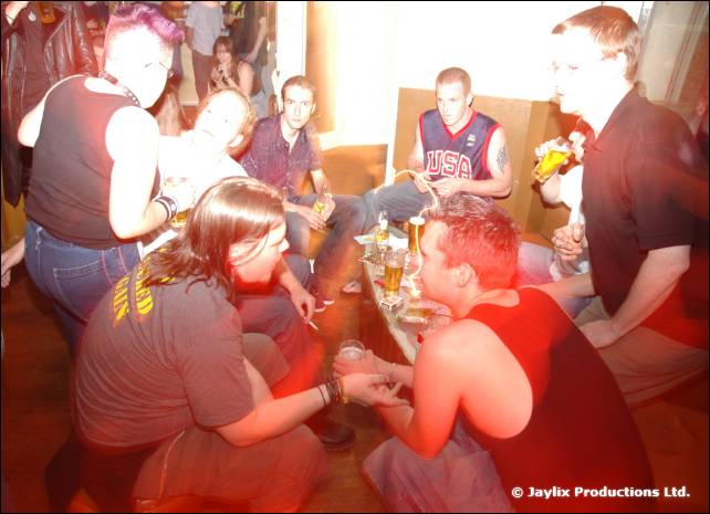 A group sit and crouch around a low table with drinks in a bar, one in a USA basketball vest