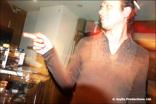 A blurred man in a brown shirt points to one side beside a microphone and equipment