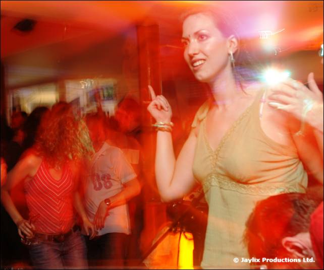 A woman in a green top raises one finger while dancing, with other dancers behind