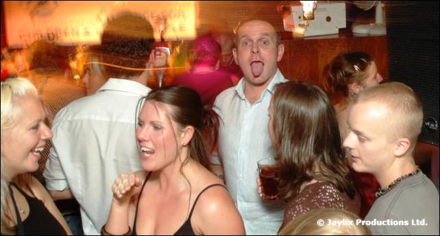 A group of people in a bar, a man at the back sticking out his tongue