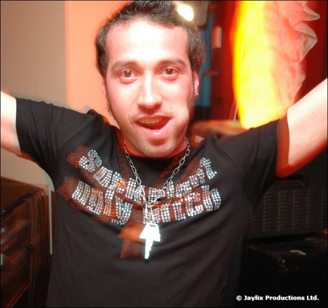 A person in a black t-shirt with a pendant holds both arms up and looks at the camera