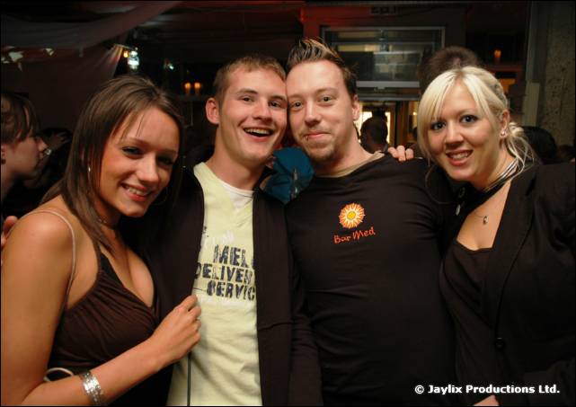 Four smiling people pose together in a bar, two women and two men