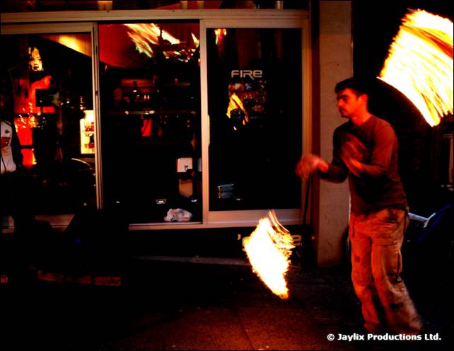 A person stands in front of a shopfront window with two blurred flames, one high and one low