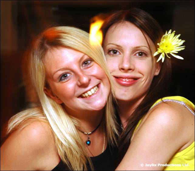 Two women smile cheek to cheek, one blonde, one with a yellow flower in her hair