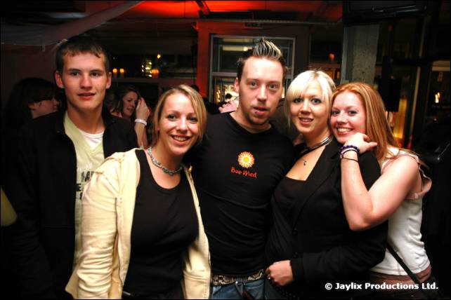 Five smiling people in dark clothes pose together in a bar