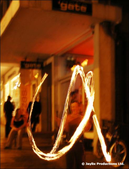 A person spins fire poi on a street outside a doorway with a gate sign