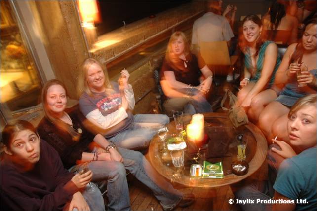 A group of people sit around a round table with a candle in a bar, some looking at the camera