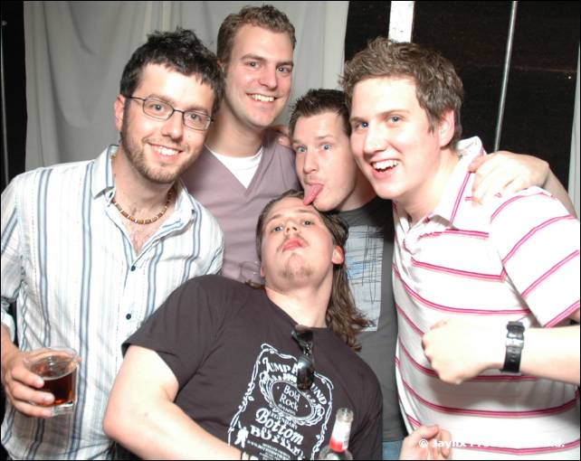 Five men crowd together for the camera, one with glasses and one sticking out his tongue