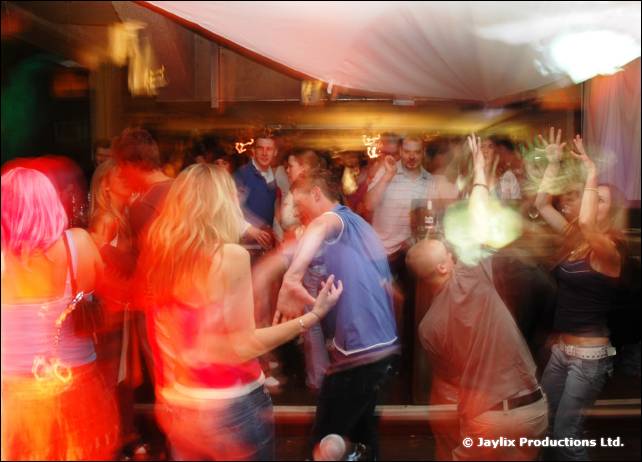 A blurred crowd dances under white draped fabric in a bar
