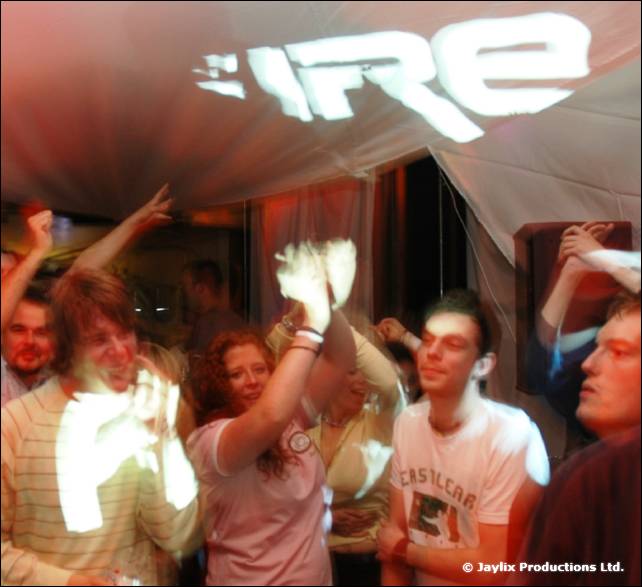 A crowd dances with raised arms beneath a white canopy with FIRE projected on it
