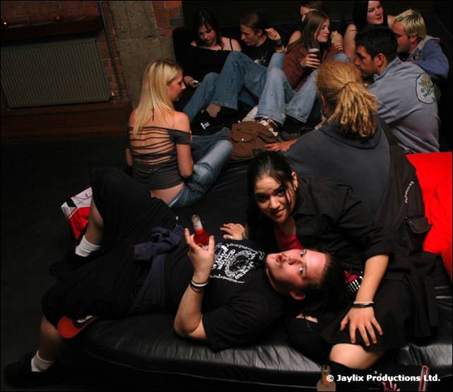 Several people lounge on a black leather sofa in a bar, two lying in the foreground