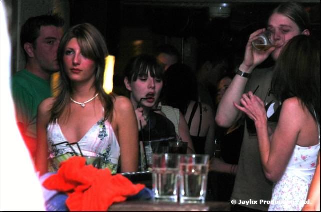 A group of people in a bar, a woman in a floral top looking at the camera, glasses on the table