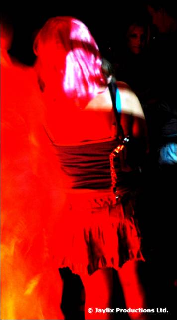 A person with pink hair seen from behind in a red dress, with flames at the left