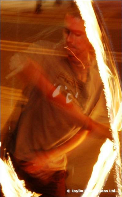 A blurred person behind a streak of fire in an orange-lit shot