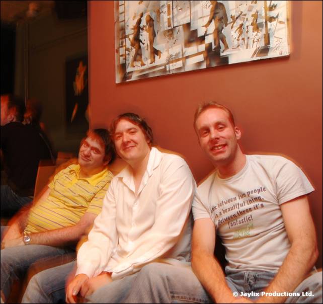 Three men sit together on a bench seat against a wall with a relief artwork