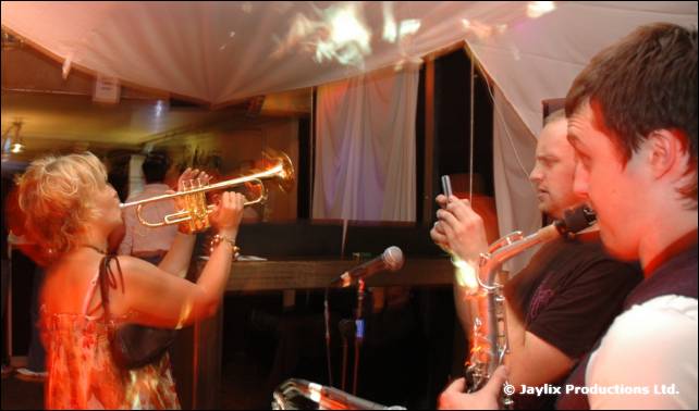 A woman plays a trumpet and two men play saxophones inside a white tent