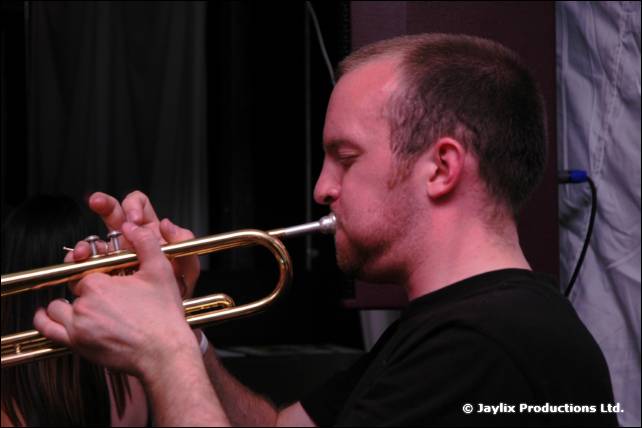 A man in a black t-shirt plays a trumpet