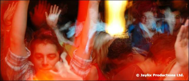 A crowd of people dance with raised hands, blurred by movement