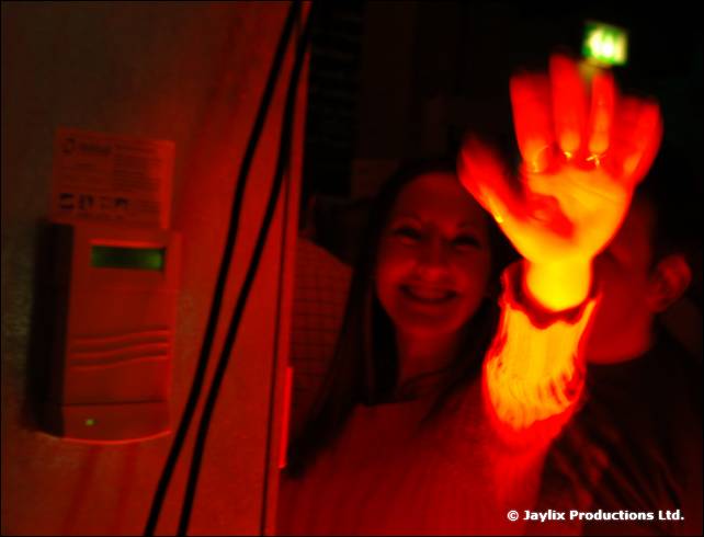 A smiling woman and a raised hand lit red in a dark corner