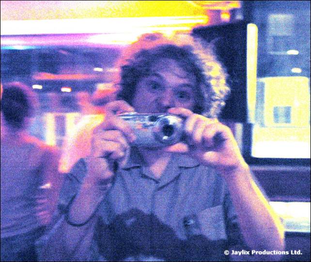 A curly-haired person holds a compact camera up to their face, in a saturated, noisy shot