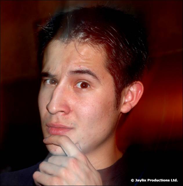 A man with dark hair rests his chin on his hand and looks at the camera