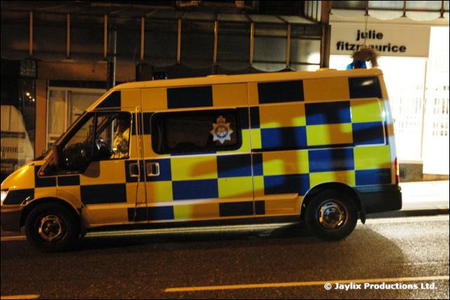 A yellow and blue chequered police van parked on a street at night