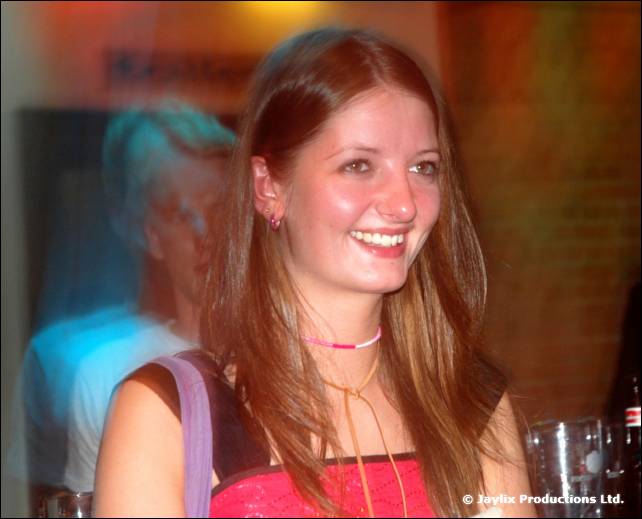 A smiling person with long hair and a pink top in a dimly lit bar
