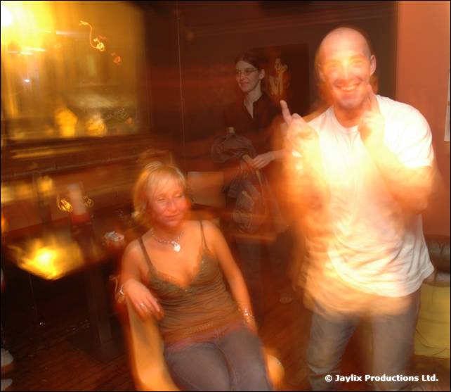 A bald man in a white T-shirt dances with a seated woman in a green top, with heavy motion blur