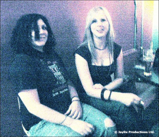 Two people sit close together, one with dark hair and one with blonde hair, in a grainy blue-tinted image